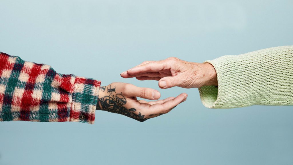 En tatoværet hånd holder hånden under en rynket hånd.
